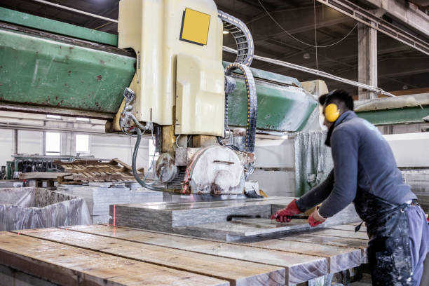 Blue-collar worker cutting granite slab on electric marble saw